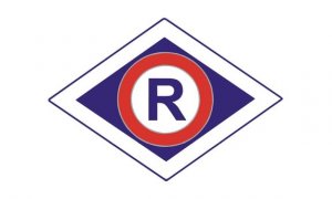 Zdjęcie przedstawia znak, oznaczenie ruchu drogowego policji tj. romb, z niebieską obwódką na białym tle a w środek wpisane jest duża litera R