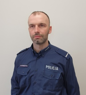 Zdjęcie przedstawia Dzielnicowego Zespołu Dzielnicowych Komisariatu Policji w Trzebiatowie w umundurowaniu służbowym bez nakrycia głowy.